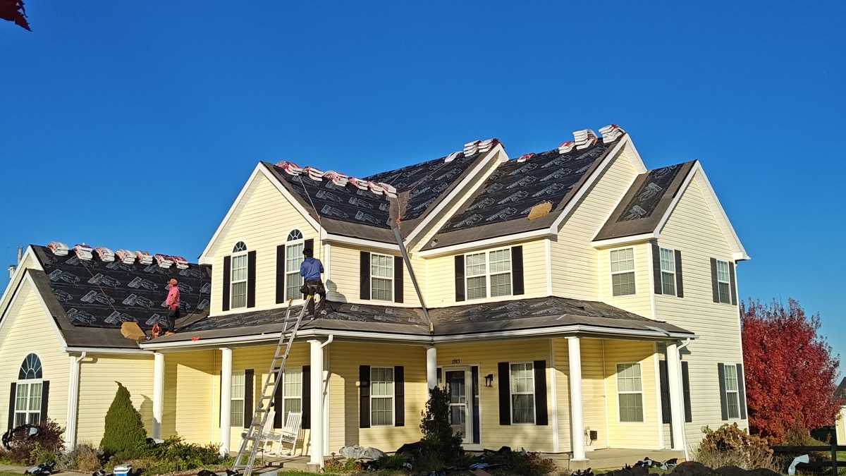 Completed roof replacement on a yellow farmhouse